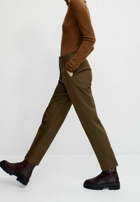 Brown turtleneck top paired with olive green, high-waisted trousers featuring straight legs and side pockets, worn with brown ankle boots.