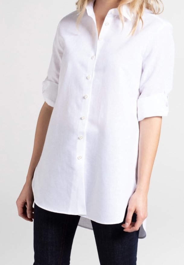 Camicia bianca con bottoni, realizzata in tessuto leggero, con colletto, maniche arrotolate e orlo curvo. Presenta bottoni simili a perle lungo la parte anteriore.