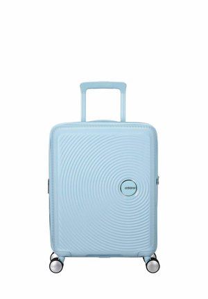 Valigia rigida di colore azzurro chiaro con design testurizzato circolare, manico retrattile superiore e quattro ruote multidirezionali.