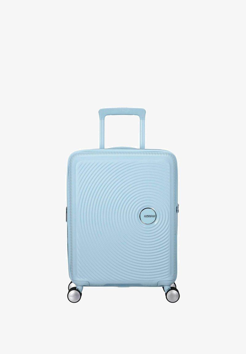 Valigia rigida di colore azzurro chiaro con design testurizzato circolare, manico retrattile superiore e quattro ruote multidirezionali.