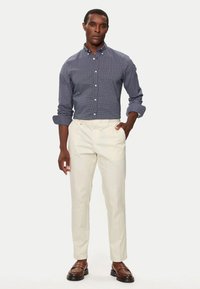 Camisa de cuadros azul marino con botones, pantalones crema y mocasines marrones. La camisa tiene cuello y mangas arremangadas. Acabado suave en general.