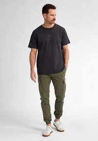 Zwart T-shirt met korte mouwen en een ronde hals, gecombineerd met olijfgroene cargobroek met zijzakken en taps toelopende manchetten. Witte sneakers maken de look compleet.