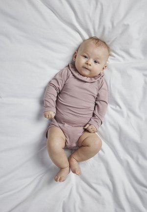 Langärmliger Babybody aus weichem, staubrosa Stoff mit rüschigem Ausschnitt, auf einer zerknitterten weißen Oberfläche liegend.