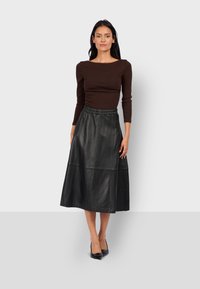 Maglietta a maniche lunghe marrone abbinata a una gonna midi in pelle nera, con cintura elastica e dettagli delle cuciture. Completato con tacchi neri.