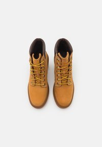 Paire de bottes de travail en cuir beige avec des lacets jaunes et marron, col rembourré marron foncé, vues de dessus sur fond blanc.