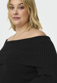 Zwarte geribbelde off-the-shoulder trui met een brede halslijn en lange mouwen, gemaakt van een rekbaar breimateriaal voor comfort.