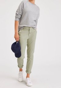 Grå sweatshirt, olivgröna byxor uppvikta vid fållarna, vita sneakers, håller en marinblå keps. Avslappnad och bekväm outfit med en lös passform.