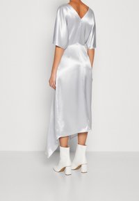 Robe midi en satin argenté avec un dos en V et des manches courtes, présentant un ourlet asymétrique et des bottes à talons blocs blanches jusqu'à la cheville.