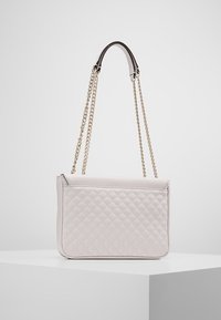 Prošité světle béžové kabelky s plochým obdélníkovým tvarem, řetízkovým popruhem a hladkou koženou texturou. Obsahuje zipové uzavření na vrchu.