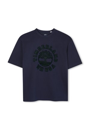 T-shirt en coton bleu marine avec un col rond et des manches courtes. Présente un logo graphique vert et le texte "Timberland USA" au centre.