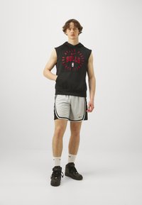 Črn brezrokavnik s kapuco z rdečim grafičnim napisom "BULLS", sivi atletski šort z črnimi akcenti, črne visoke teniske, bele nogavice.