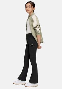 Giacca atletica grigia, top bianco, pantaloni neri a zampa d'elefante con logo, abbinati a sneakers bianche. Tessuto morbido, stile casual, design aderente.
