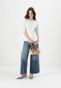 Sudadera gris con un dobladillo peplum, vaqueros de pierna ancha azul, tacones de punta taupe y un pequeño bolso metálico con un asa trenzada.