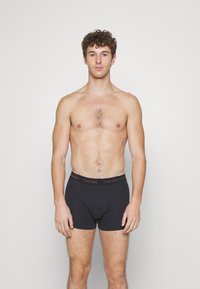 Svarte boxershorts med Calvin Klein-logo i midjen. Myk stoff, tettsittende design og lengde til midten av låret med glatt tekstur.