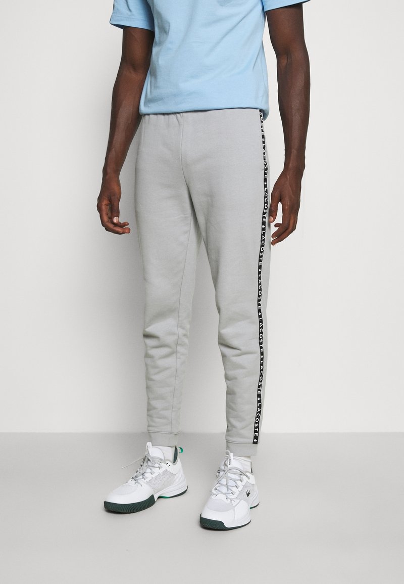 Grå bomulds-sweatpants med en sort logostribe i siden, slim fit, kombineret med hvide sportssko og en lyseblå t-shirt.