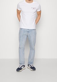 Bílá košile s krátkým rukávem s logem "HILFIGER", světle modré džíny a tmavé tenisky s bílými akcenty. Jednoduchý, neformální outfit.