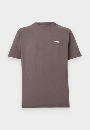 Καφέ κοντομάνικο μπλουζάκι με στρογγυλή λαιμόκοψη και μικρό λευκό λογότυπο "OBEY" στο αριστερό πάνω μέρος του στήθους.