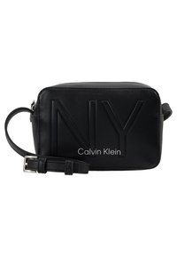 Borsa a tracolla in pelle nera con logo "NY" inciso e stampa "Calvin Klein" sul fronte. Presenta una tracolla sottile e forma rettangolare.