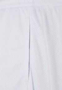 Shorts de sport en mesh blanc, présentant un design léger, une texture avec de petits trous respirants et une taille pour le confort.