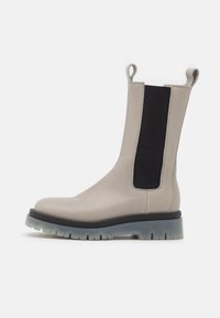Stivali ankle in pelle grigia con pannelli elastici neri, linguette ed una suola in gomma spessa con finitura grigia traslucida.