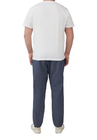 Witte t-shirt met korte mouwen, gecombineerd met marineblauwe broek met een subtiele textuur, aangevuld met lichtgekleurde schoenen.