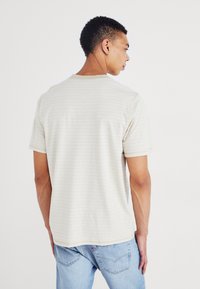 Béžové pruhované tričko s krátkym rukávom vyrobené z jemného materiálu, s okrúhlym výstrihom a voľným strihom, skombinované so svetlomodrými džínsami.