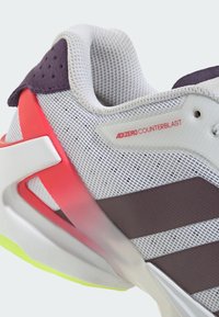 Gros plan sur la chaussure de course adidas Adizero Counterblast avec un filet blanc, des rayures violettes et un détail de soutien au talon rouge.