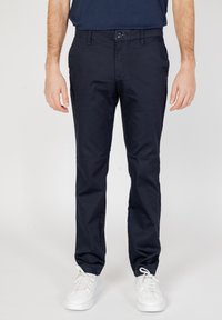 Chino in cotone blu navy con design a gamba dritta, tasche frontali, chiusura con bottone e una texture liscia, abbinati a sneakers bianche.