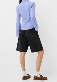 Jasnoniebieska koszula w paski z długim rękawem, zestawiona z czarnymi szortami dżinsowymi i brązowymi butami żeglarskimi, w połączeniu z białymi skarpetkami i luźnym krojem.