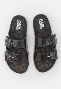 Sandales noires transparentes avec deux boucles ajustables, semelle intérieure à motif hexagonal et logo en relief. Fabriquées en matériau synthétique durable.