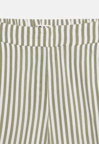 Κοντινό πλάνο σε πράσινο και λευκό ύφασμα με κάθετες ρίγες, με ζώνη μέσης και λεπτομέρειες ραφής.