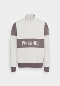 Sudadera gris claro con media cremallera, detalles en ribete gris oscuro y el texto bordado "PEGADOR" en el pecho. Material de mezcla de algodón suave.