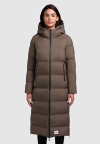 Lång puffjacka i ett matt mörkbrunt material med huva, framsida med dragkedja och sidofickor. Har horisontellt quiltade sektioner.