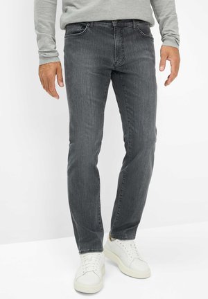 Jeans in denim grigio scuro con una vestibilità slim, caratterizzati da leggere sfumature e un classico design a cinque tasche. Indossati con sneakers bianche.