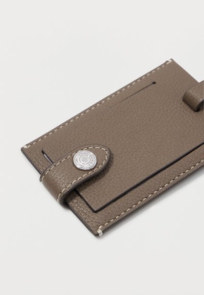 Καφέ δερμάτινη θήκη καρτών με υφή, αντίθετο ράψιμο και κλείσιμο με κουμπί που έχει κυκλική ασημένια λεπτομέρεια.