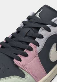 Κοντινή λήψη μαύρου, ροζ, γκρι και μπεζ αθλητικού παπουτσιού με μαύρα κορδόνια, εμφανές το λογότυπο της Nike και το λογότυπο Jumpman στη γλώσσα.