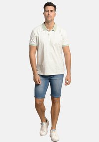 Camisa polo de manga corta, verde claro y blanca, con cuello, combinada con pantalones cortos de mezclilla. El conjunto presenta patrones simples y zapatillas blancas.