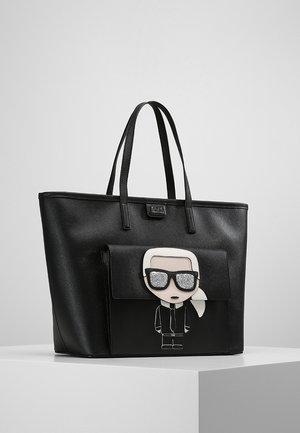 Czarna torba na ramię z podwójnymi uchwytami i przednią kieszenią, na której znajduje się rysunkowa postać z błyszczącymi okularami przeciwsłonecznymi i kucykiem.