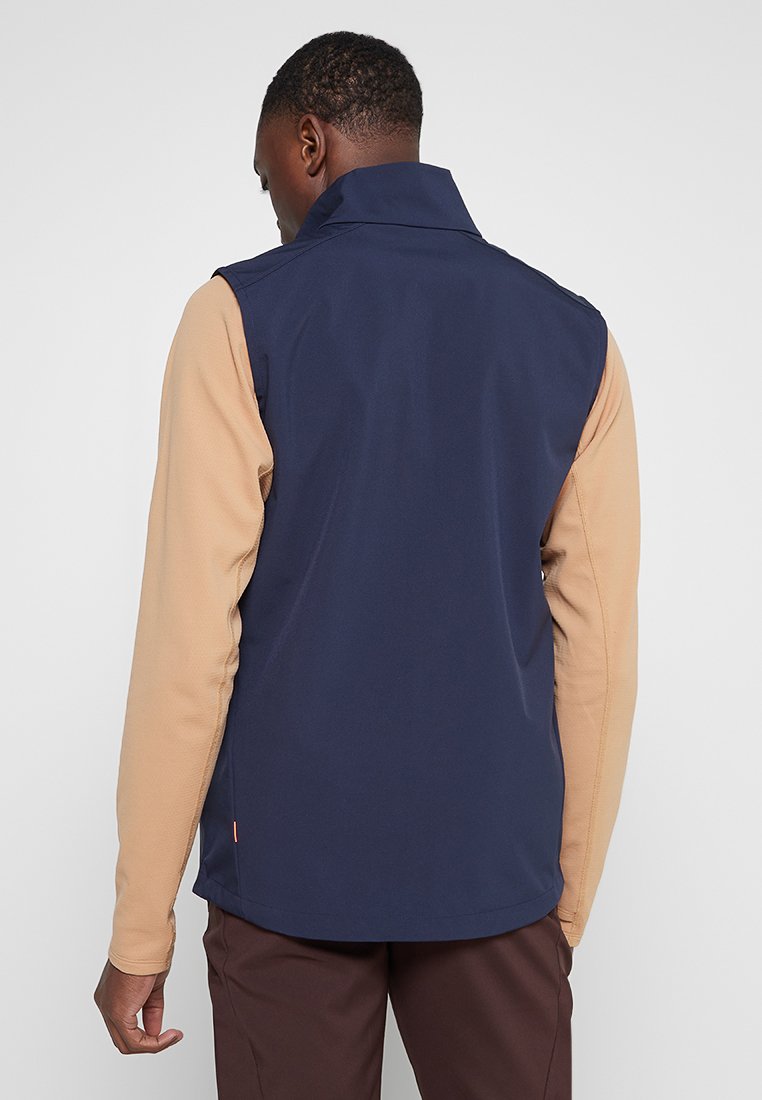 Granatowa kamizelka z beżowymi rękawami, charakteryzująca się wysokim kołnierzem i gładką teksturą. Widok z tyłu ukazuje dopasowany krój i minimalistyczne detale.