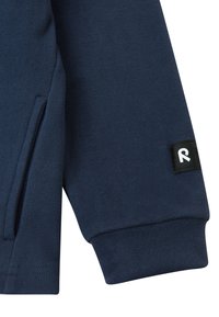 Manica di felpa blu navy con tasca laterale, polsino a costine e un piccolo etichetta nera con una lettera "R" bianca.