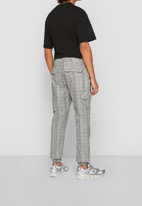 Grijze geruite cargobroek met een tapered fit, zijzakken en een elastische boord. Gecombineerd met een zwart T-shirt en grijze sneakers.