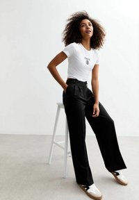 Vit formad t-shirt med "PARIS" tryck, kombinerad med högmidjade svarta vida byxor och vita sneakers med bruna sulor.