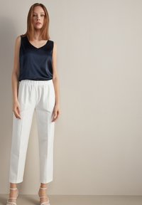 Granatowa satynowa bluzka bez ramiączek z dekoltem w kształcie litery V, w zestawieniu z białymi spodniami z elastycznym pasem oraz białymi sandałami na cienkich paskach. Prosty i elegancki design.