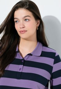 Lilla og marineblå stribet polo med krave og treknapslukning. Blødt stof med en tætsiddende pasform og glat tekstur.