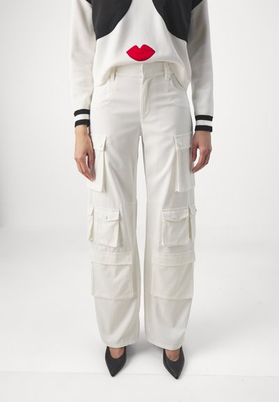 Pantalons cargo blancs avec de multiples poches avant, une coupe décontractée et des bas de pantalon à revers. Portés avec un pull noir et blanc orné d'un design de lèvres rouges.