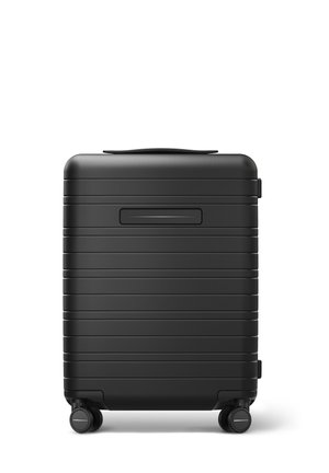 Valise rigide noire avec des rayures horizontales, poignée supérieure et quatre roues pour la mobilité. Dispose d'une fente horizontale pour une pièce d'identité ou des étiquettes.