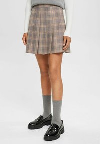 Falda plisada a cuadros en tonos gris, rosa y amarillo, hecha de una tela ligera. Combinada con calcetas grises y mocasines negros brillantes.