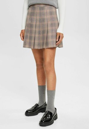 Jupe plissée à carreaux dans des tons de gris, rose et jaune, fabriquée en tissu léger. Associée à des chaussettes grises et des mocassins noirs brillants.