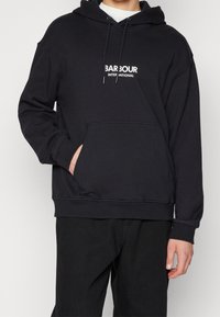 Černá mikina s kapucí z bavlněné směsi, s přední kapsou, kapucí na stahovací šňůrku a bílým logem "BARBOUR INTERNATIONAL" na hrudi.
