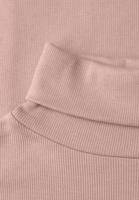 Geribbelde stof in zachtroze, met een hoge halslijn en een gladde textuur. Het materiaal heeft een subtiele glans en een uniform patroon.